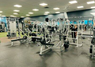 A well-equipped gym with various weight training machines and barbell setups.