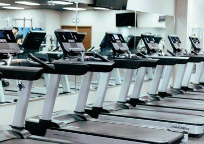 A row of treadmills with digital displays in a modern gym, unoccupied and lined up facing the mirrored wall.