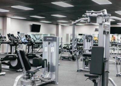 Modern gym interior featuring a variety of exercise equipment including treadmills, weight machines, and stationary bikes, in a clean and organized setup with grey and black tones.