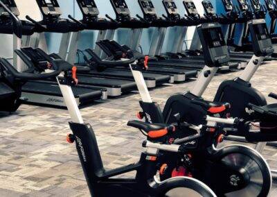 A row of stationary bikes in the foreground with treadmills inside a gym.